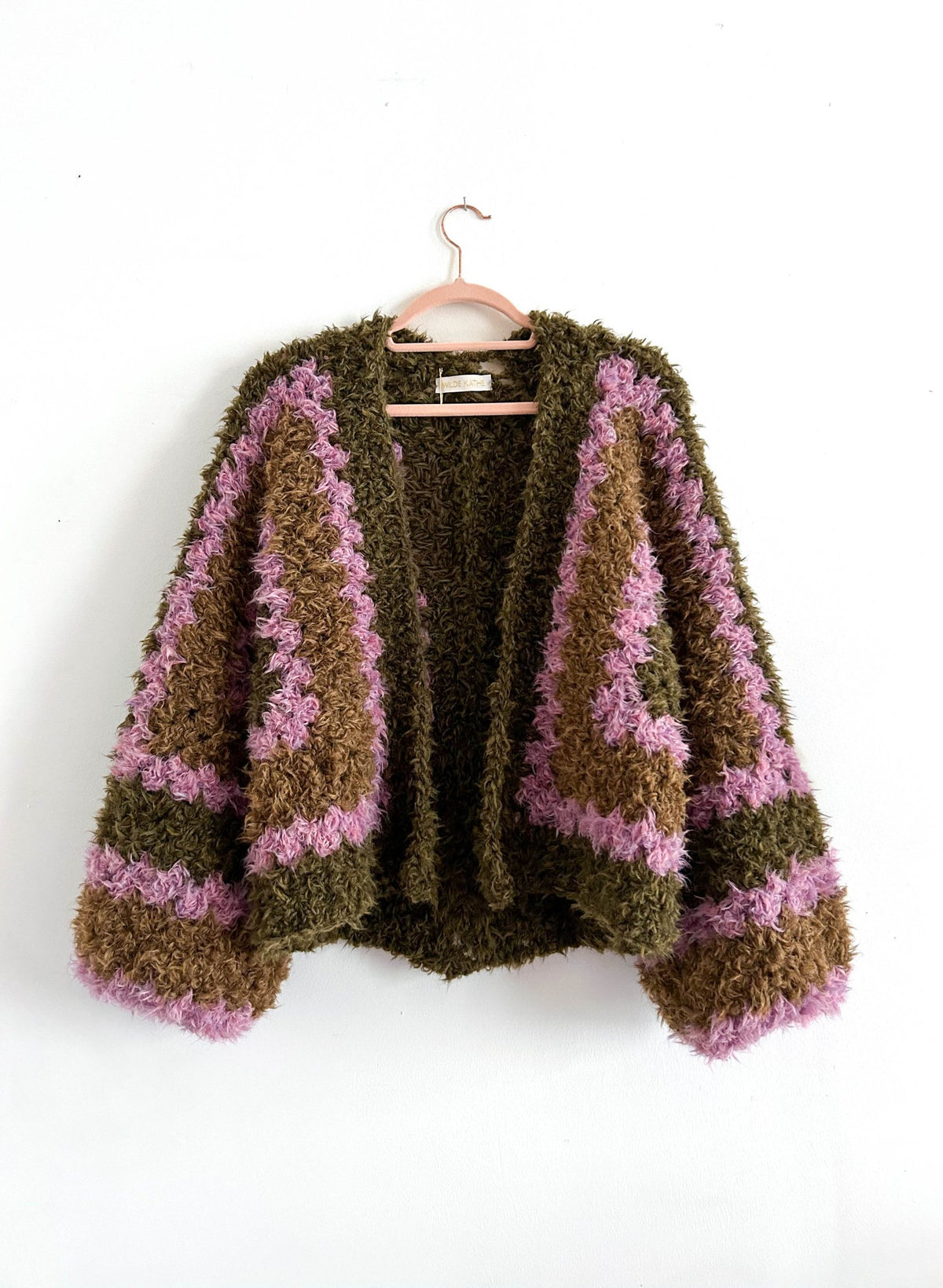 Vorderansicht der olivgrünen Alpaka-Strickjacke für Damen mit rosa-braunen Bogenmustern und weiten Ärmeln auf einem Bügel