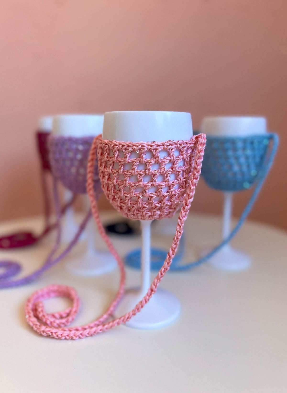 Rosa Weinglashalter mit Pailletten als Geschenk für den Junggesellinnenabschied, dahinter Flieder, Beere und Hellblau
