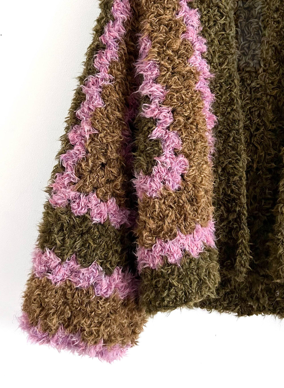 Detail der Kunstfellstrickjacke: langflorige Oberfläche in Olivgrün, Braun und Rosa am Ärmelende
