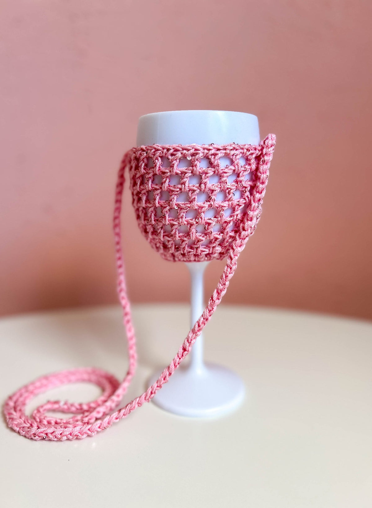 Weinglashalter in Rosa mit roséfarbenen Pailletten an einem weißen Weinglas, der Träger liegt in Schlaufen davor